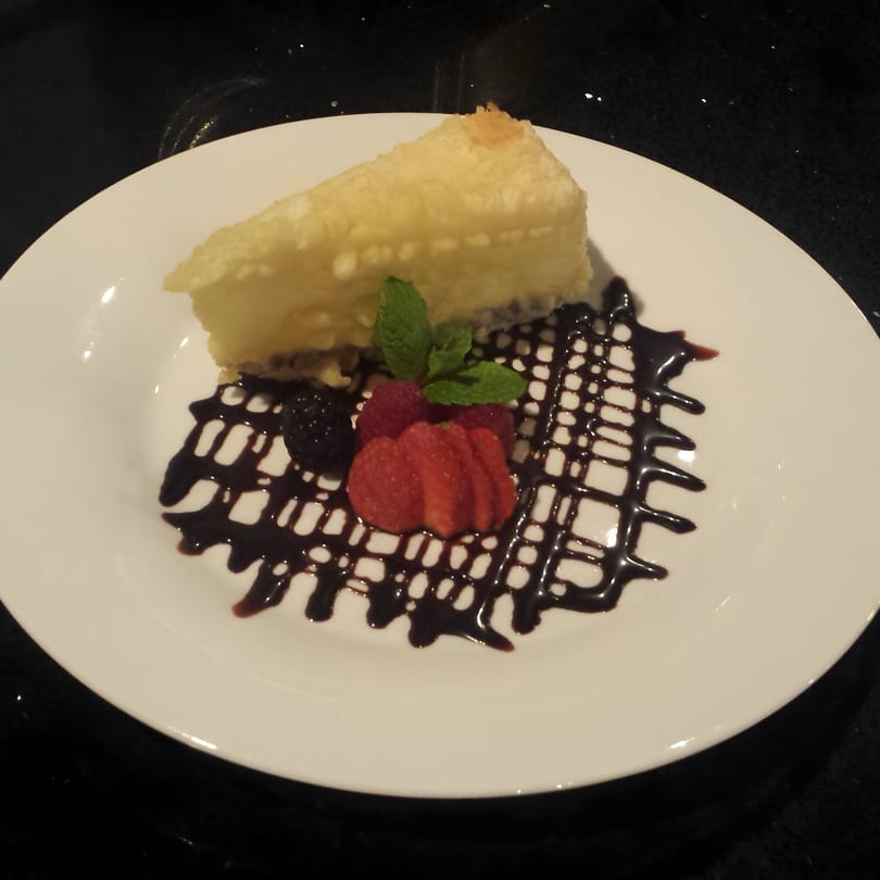 Tempura cheesecake with chocolate drizzle, fresh strawberries, raspberries, and mint on a white plate.