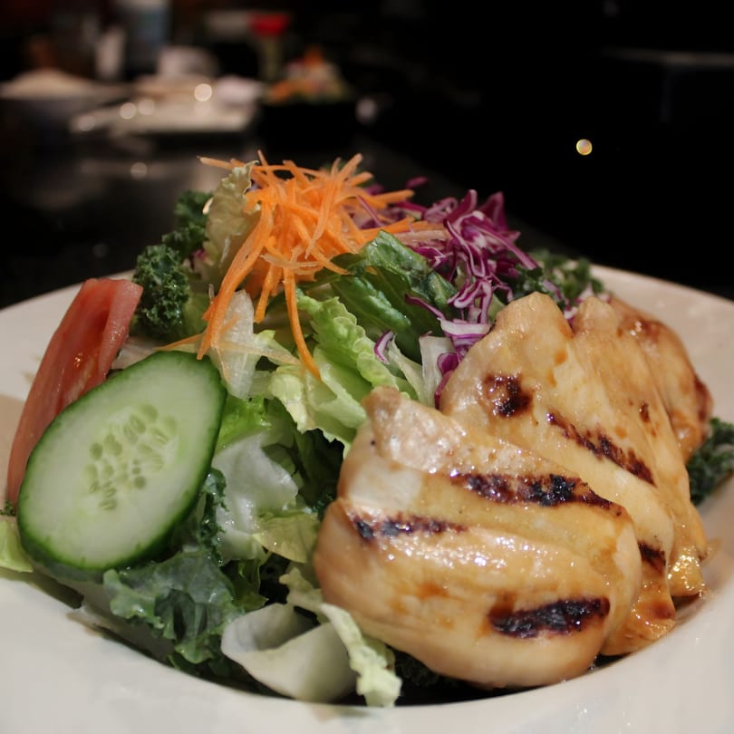 Grilled chicken breast slices on a fresh garden salad with lettuce, carrots, cucumber, and tomato.